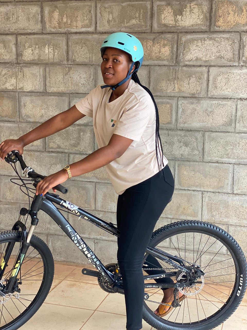 Rider in a teal helmet posing with her mountain bike against a stone wall