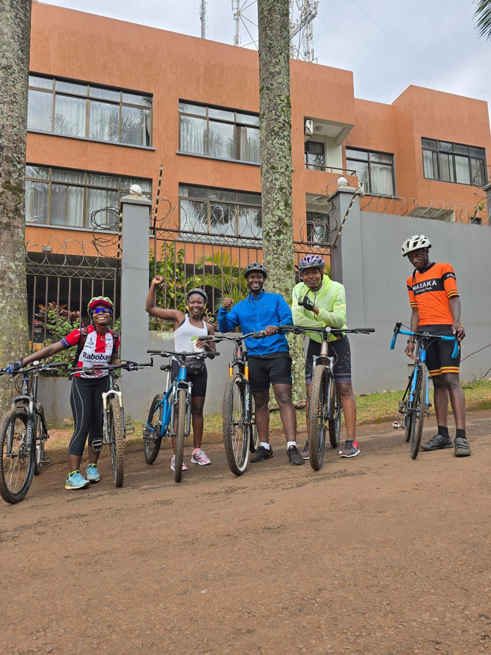 Group of five cyclists posing with their bikes outside an office building